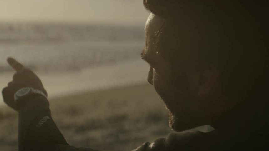 A close up of a mans face as he looks out over the ocean and points