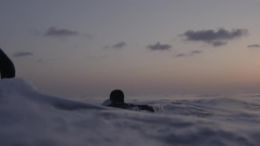 Father teaching son how to ride a surfboard in the ocean at evening
