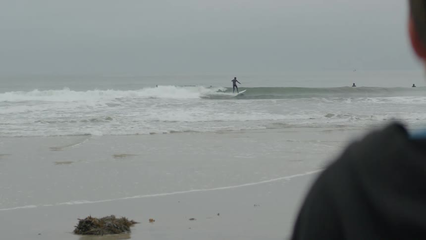 Boy standing on a beach watches people surfing on the ocean waves
