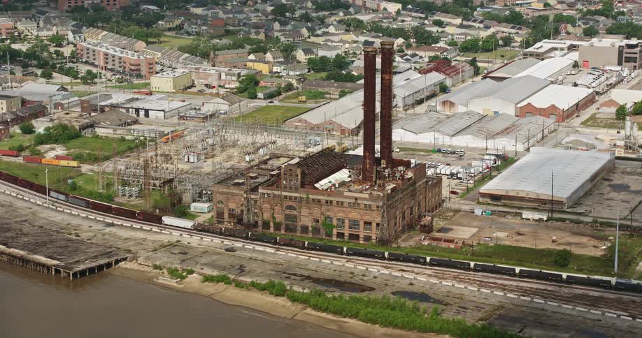 Approaching aerial view of a power generating station in the Garden District of New Orleans alongside the riverfront during a partly cloudy day
