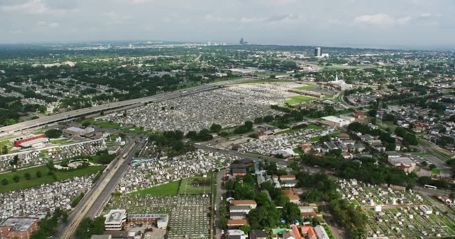 An aerial view of several historic cemeteries in Lakeview New Orleans surrounded by lush greens during a partly cloudy day