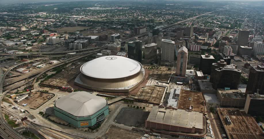 A stunning 4K aerial view of the Superdome New Orleans Arena and downtown skyscrapers in Louisiana with partly cloudy skies and the Mississippi River visible shot during the daytime in summer