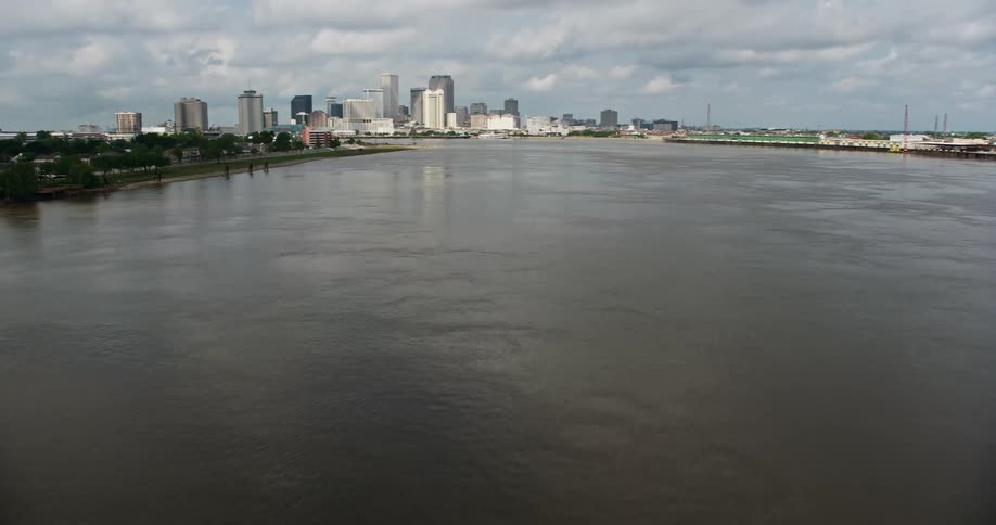 A low altitude 4K aerial view of approaching Downtown New Orleans skyline over Mississippi River during a partly cloudy day