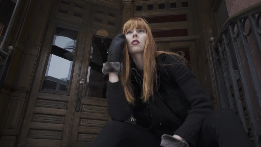 A woman sitting on building's stoop moves her hand to her chin