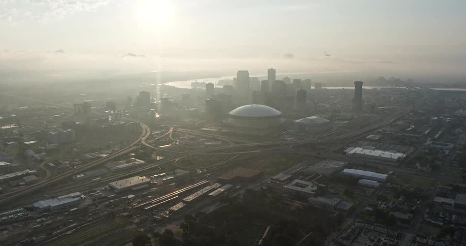 Aerial footage of the Louisiana Superdome and Downtown New Orleans at sunrise approaching from Mid-City on a hazy morning