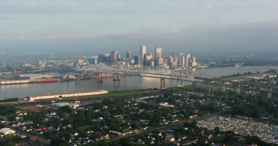 An aerial view of two large bridges spanning a river at sunrise surrounded by the metropolis of Downtown New Orleans
