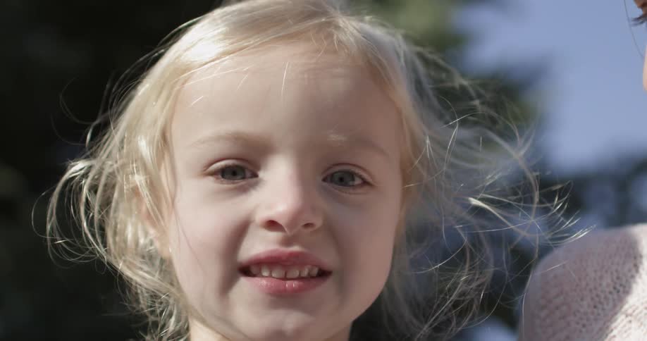 A blond girl smiles and sniffs a stick