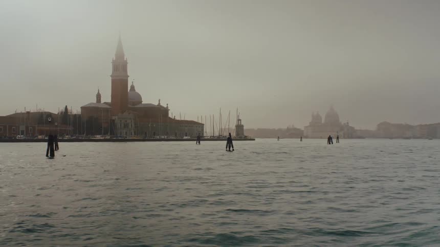 A building with a spire comes into view over the water on a cloudy day
