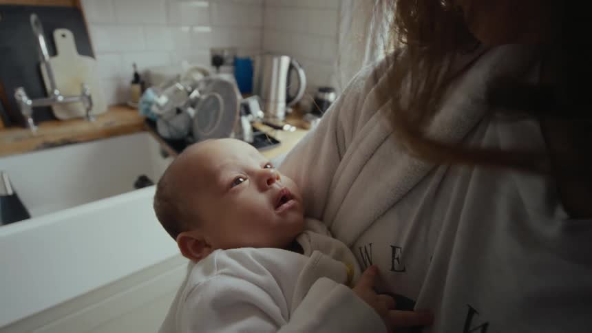 Mother holding her newborn baby in her arms near the kitchen sink at home