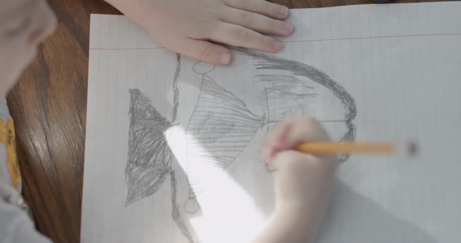 A child uses a pencil to color and draw on a piece of paper
