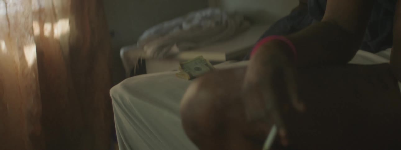 A person puts money on a chair arm next to a person smoking a cigarette