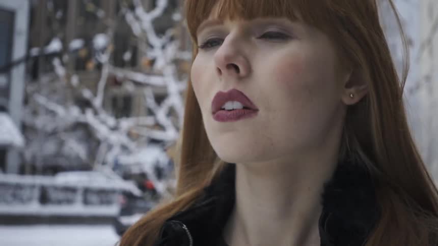 A woman flips her hair back and adjusts her coat collar