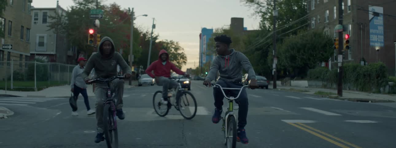 A group of young men rides their bikes down the street