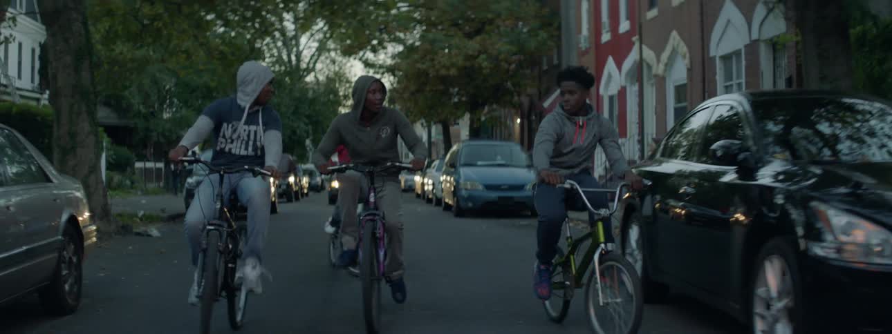 A group of teenagers ride bikes down a busy city street