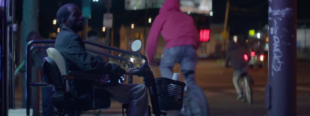 A man is sitting as people pass him on a street at night
