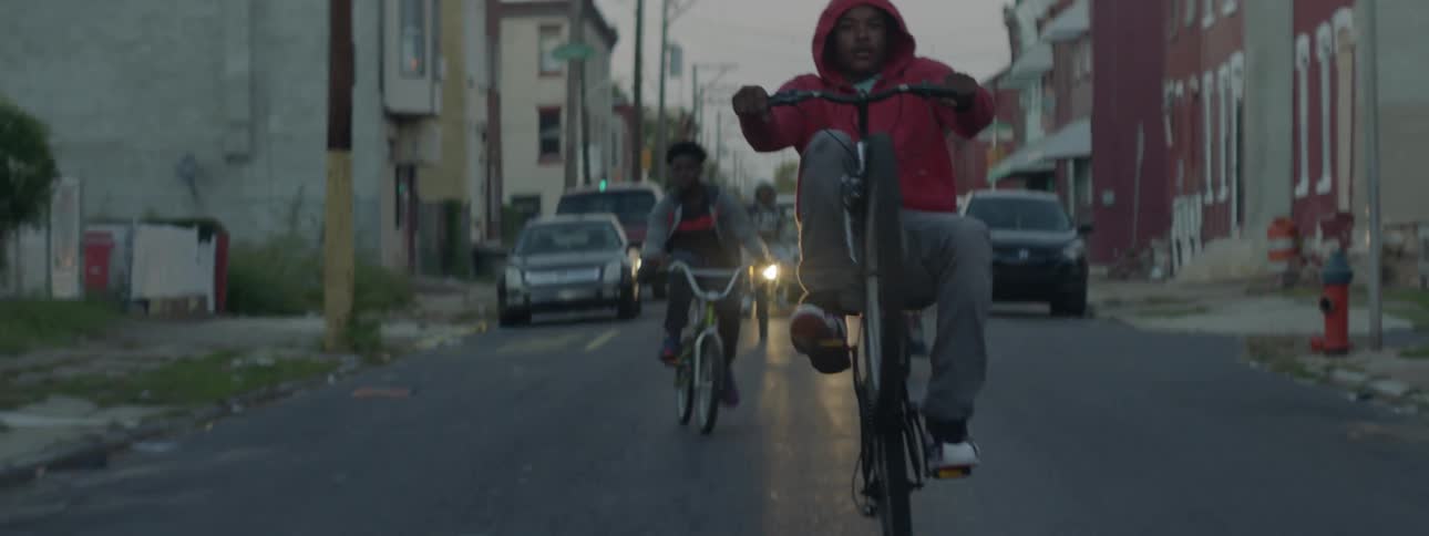 A group of bikes ride down a street one is doing a pop wheelie