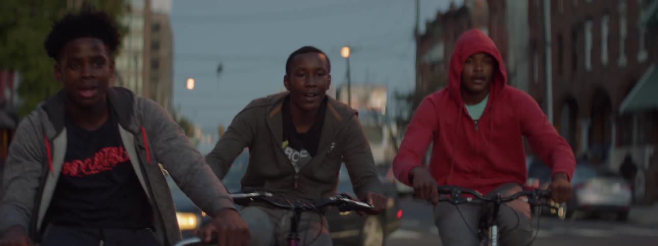 Three people ride their bikes down a street at sunset