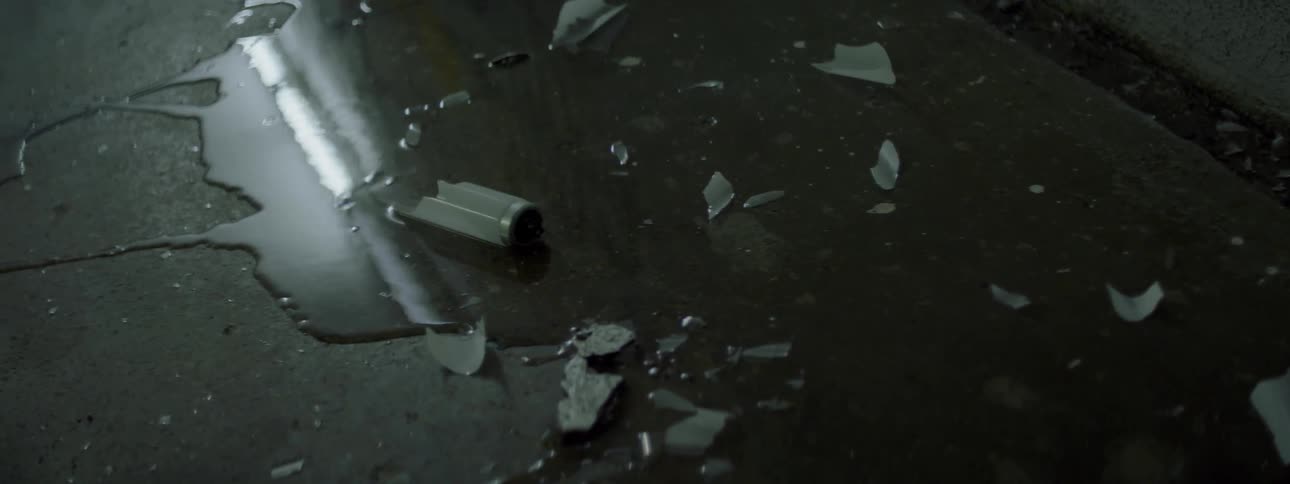 A puddle is covered with broken glass from a bulb