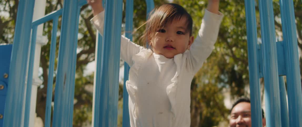 A father is playing with his little girl in the park as she holds on to the rail bar with her hand