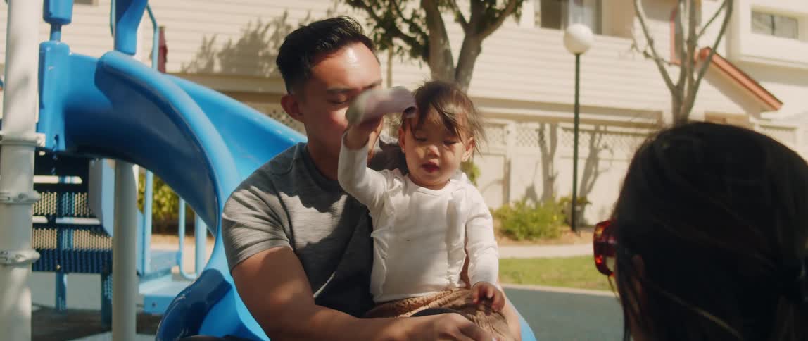 Father sits on a slide with his daughter on his lap while he puts socks and shoes on her feet as the mother sits in front of them