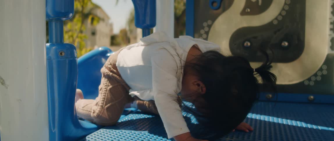 Baby toddler girl at the top of kiddy slide turns over on belly and slides down backward