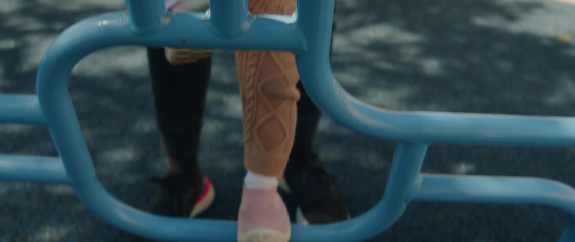 A father holds his toddler daughters hands as he helps her climb blue playground bars