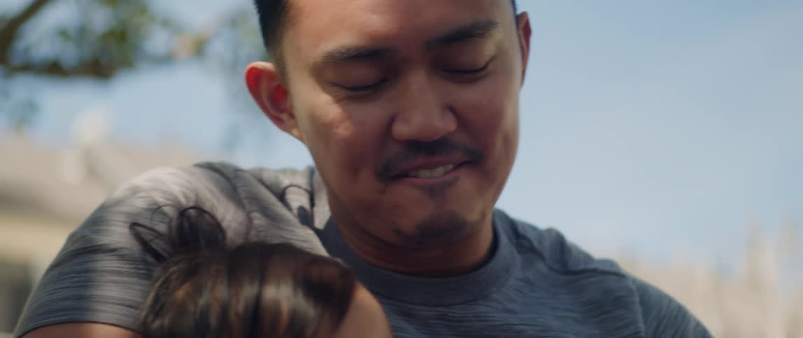Happy caring father sitting under a tree outdoors holding his daughter in his arms
