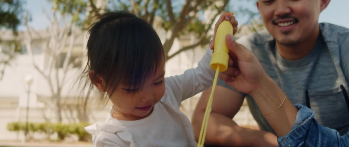 Father and toddler daughter create bubbles out of a bubble ring that the mother holds