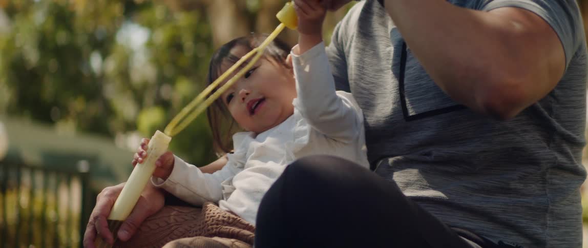 A father holds his daughter as she blows bubbles with a wand