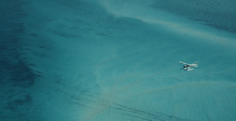 An aerial of a small white air plane flying over a blue ocean