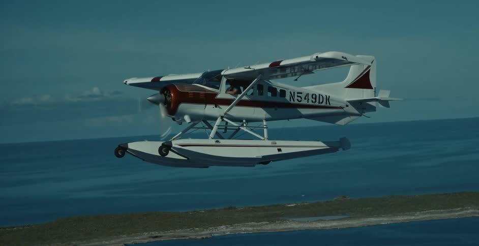 Seaplane coming in for landing while traveling at low altitude over blue sea near shoreline