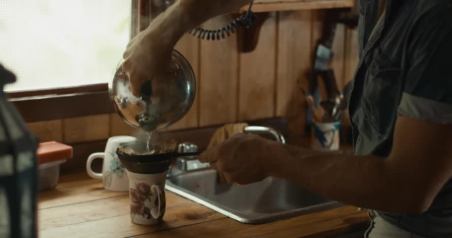 Man stands near sink pouring water from kettle over coffee grounds in lined sieve