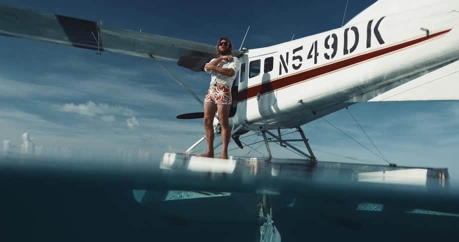Man stands on pontoon of floating airplane bobbing on reflective water