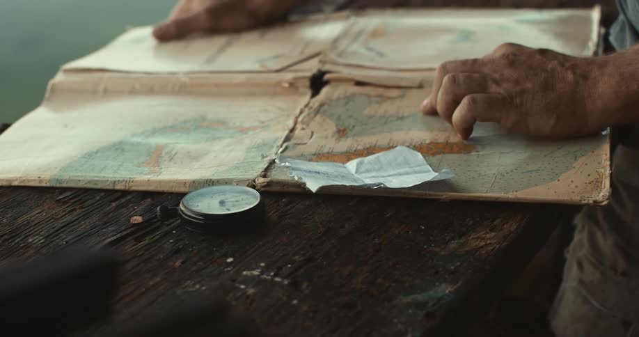 Close up of the hands of a man unfolding a map next to a compass to find a place
