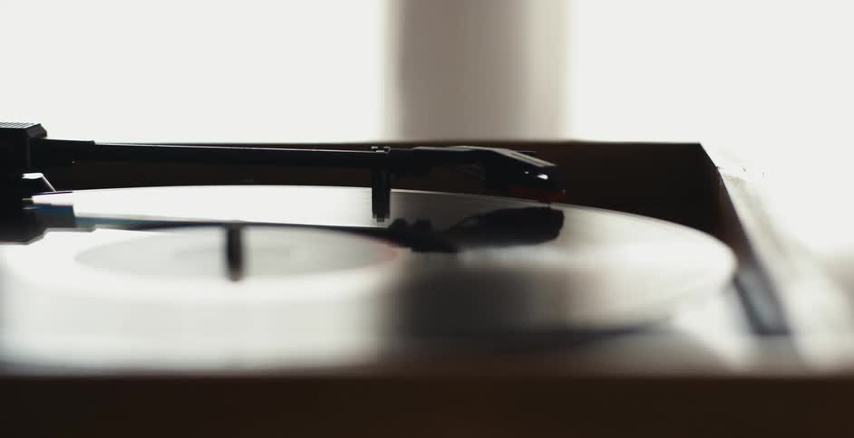 Close up of the hand of a person placing the turntable arm over a vinyl record