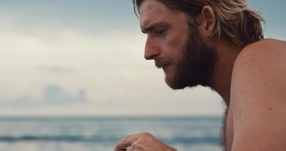 A man sitting without a shirt on spitting into goggles and looking down at the ground