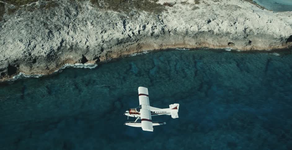 An aerial of a white airplane flying over waters near rocky cliffs