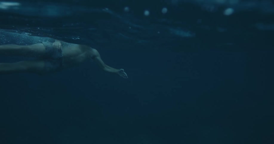 A man swimming underwater and then rising to the surface with black flippers on his feet