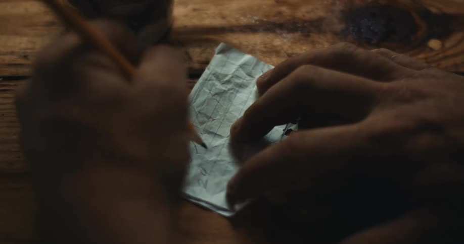 Close up of the hands of a person hand writing with a pencil over a crumpled piece of paper