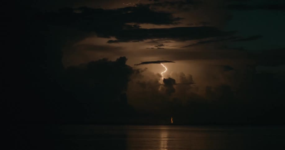 Lightning strikes on horizon over the water brightens the cloudy night