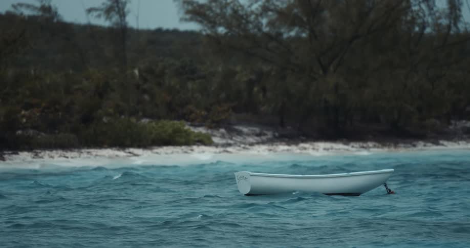 Boat anchored near strip of beach backed by wilderness bobs on ocean waves
