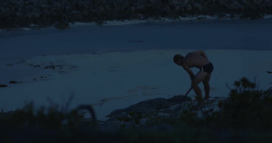 A man shoveling sand on the beach at dusk