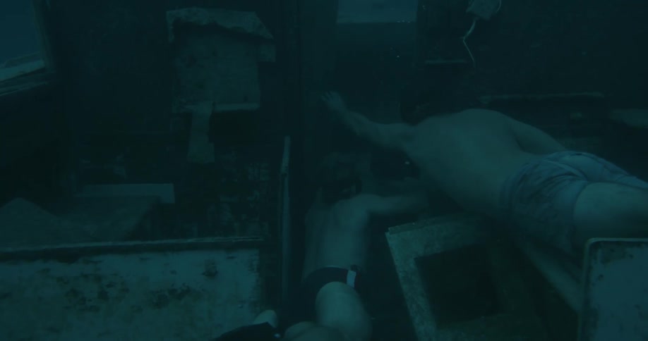 Underwater footage of two young muscular men wearing swimsuits entering the cabin of a shipwreck
