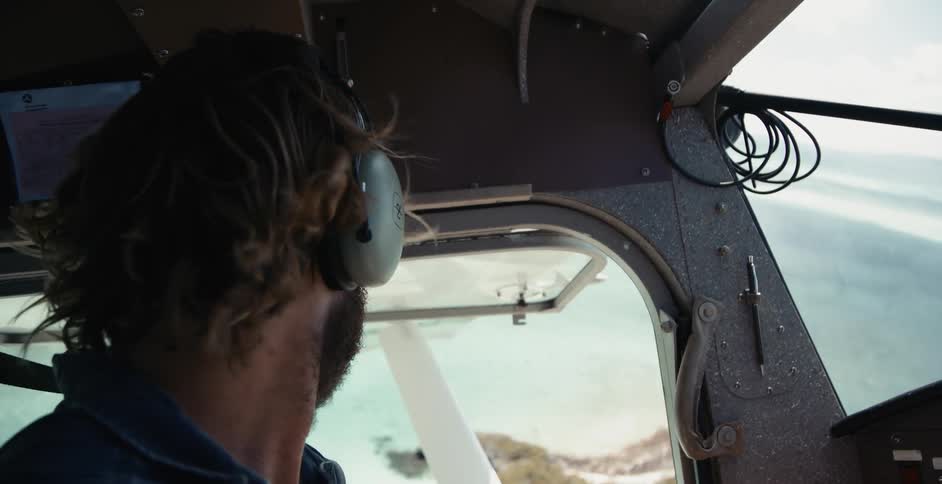 A close up of a pilot flying a plane with headphones on over ocean and beach islands
