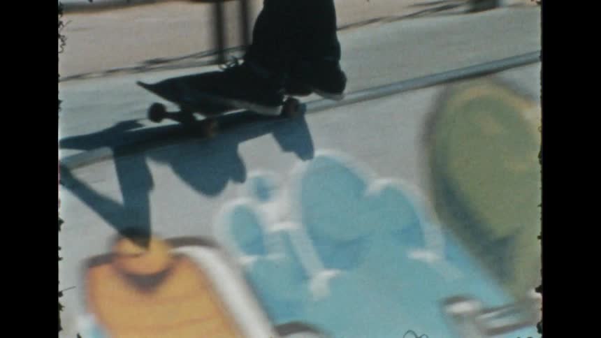 Skateboarder rides up skate park bowl decorated with colorful graphic before riding along rim and down again