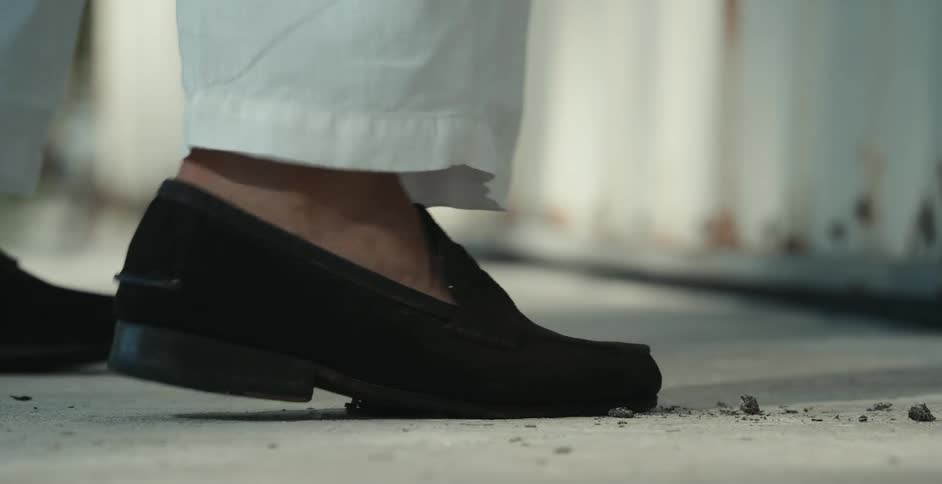 A man throws a smoking cigar on the ground and only his shoed foot is shown twisting on it to extinguish it