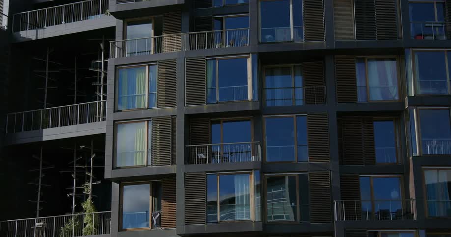 Clear shiny apartment building windows reflect the sky and an opposing building