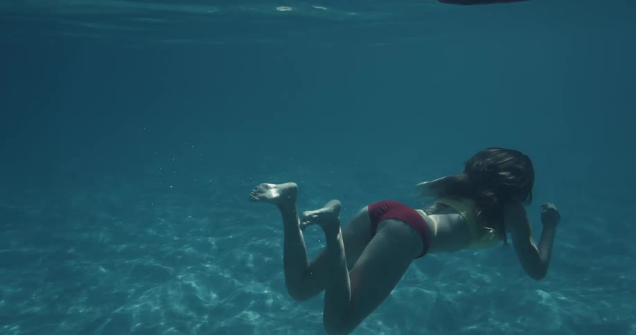 A woman swimming underwater and swimming to the surface