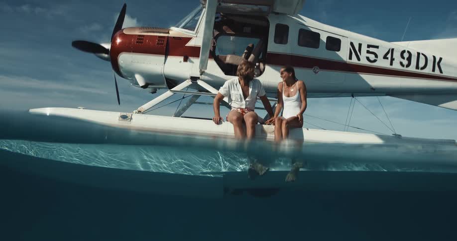 Romantic couple sit on the float of a seaplane in the ocean while kissing