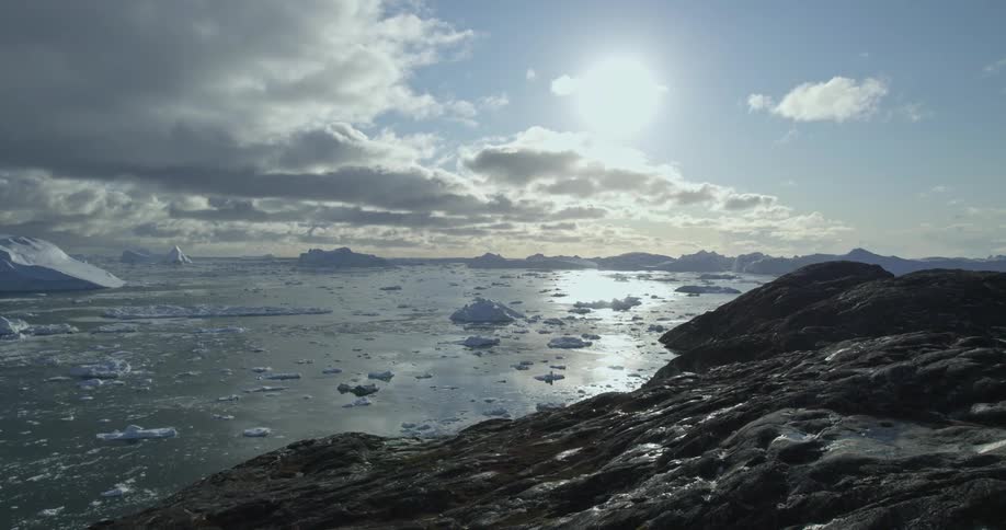 An aerial view of an ocean with icebergs and glaciers in it alongside rocky mountains